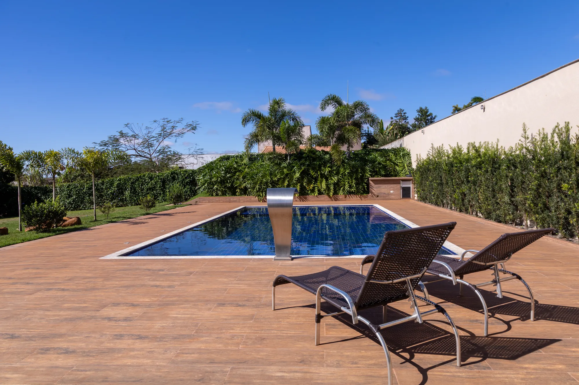 Piscina de pastilhas azuis com cascata, deck amadeirado e espreguiçadeiras pretas